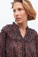 Blusa negra con estampado floral en tonos rosados y rojos, cuello con volados y mangas largas con puños elásticos.