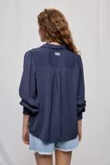 Camisa de manga larga color beige con cuello clásico y botonadura frontal. Presenta mangas con volumen sutil, puños abotonados y una silueta amplia de caída fluida.