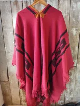 Poncho rojo con diseño geométrico en negro y detalles en marrón en el cuello, terminado con flecos en los bordes.