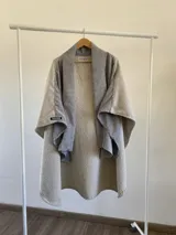 Ruana de diseño estructurado confeccionada en tela tipo tapiz con textura rugosa en color beige, con solapas amplias en tejido de cuadros vichy gris y blanco.
