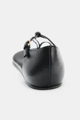 Sandalia plana de piel color negro, con tira fina que pasa entre los dedos y detalle de nudo trenzado. Posee una tira trasera ajustable con hebilla metálica dorada y suela fina.