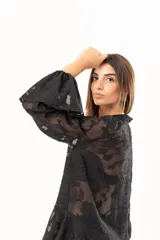 Blusa negra de tejido semitransparente con diseño floral en relieve, cuello alto con lazo frontal y mangas largas con volados en los puños.