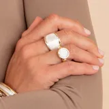 Anillo de diseño circular con centro de nácar y borde texturizado en tono dorado, montado sobre una banda de plata.