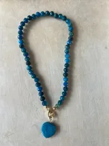 Collar con dije de corazón facetado en color verde esmeralda, con cadena de cuentas de cristal facetadas en tonos amarillos y dorados.