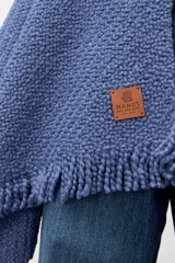 Ruana de tejido de punto con textura, color azul, con terminaciones de flecos en los bordes. Diseño envolvente y holgado.