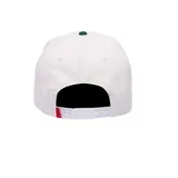 Gorra de béisbol blanca con parche frontal de vaca lechera y la palabra "Cash". Visera curva con costuras zig-zag verdes y detalle de cuerda trenzada verde en la base de la copa.