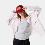 Camisa de manga larga con cuello y botones frontales, corte boxy, en color blanco con estampado de cuadrícula fina en tono rosado. Presenta un pequeño logo bordado en rojo en el pecho.