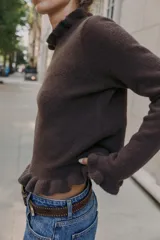 Jersey de punto color marrón con cuello redondo, manga larga y detalles de volantes en el cuello, puños y ruedo.
