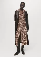 Vestido midi de corte recto con estampado animal print de cebra en tonos marrón y beige. Presenta cuello camisero, cierre frontal con botones, mangas cortas con dobladillo y un cinturón tipo batín para ajustar a la cintura.