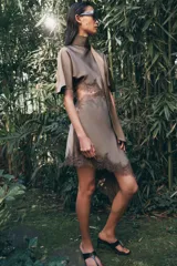 Vestido midi satinado de cuello subido y manga corta tipo capa. Presenta aberturas laterales con aplicación de encaje a tono y bajo asimétrico con detalle de encaje. Incluye un pañuelo integrado en el mismo tejido y cierre posterior con botones forrados.