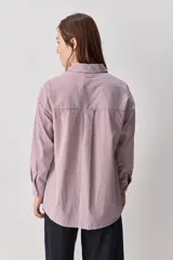 Camisa de calce relajado con diseño a rayas verticales en tonos azul y blanco, cuello clásico, mangas largas con puños abotonados y cierre frontal con botones. Presenta bolsillos aplicados en el delantero y una silueta versátil.