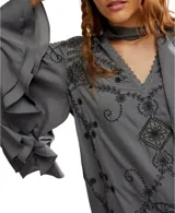 Vestido corto gris con bordados negros, mangas anchas con volados y lazo al cuello.