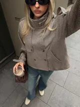 Chaqueta corta de corte recto con estampado de pata de gallo en tonos marrones y beige. Presenta cuello alto, cierre frontal cruzado con botones y detalles de trabillas en los hombros y puños.