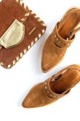 Zapatos tipo zueco de gamuza negra con punta fina y tira sobre el empeine decorada con tachas metálicas plateadas. Posee taco cuadrado de madera y suela con plataforma.