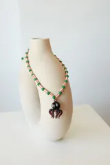 Collar corto con cuentas de plástico amarillas y verdes, y dije de vidrio con forma de pulpo negro.