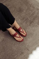 Sandalia plana de cuero color rojo, estilo chinela, con tiras finas adornadas con microtachas doradas. Posee tira de sujeción al tobillo con hebilla.