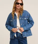 Campera de jean azul de corte amplio, con cuello clásico, cierre frontal con botones metálicos, mangas largas y bolsillos con solapa en el pecho.