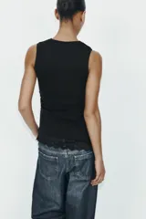 Camiseta ajustada (slim fit) color crema, con cuello redondo y mangas sisa. Presenta frunces laterales y un bajo asimétrico con detalle de encaje a tono.