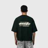 Remera de corte oversize color verde oscuro, con estampa gráfica en la espalda que incluye texto y diseño lineal.