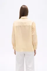 Camisa de algodón color blanco, de corte holgado y manga larga. Presenta detalles de encaje tipo puntilla en el frente, espalda y mangas, con cierre frontal de botones y cuello camisero clásico.