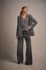 Blazer gris con rayas verticales finas, de calce amplio, con cruce recto y acceso por medio de un botón. Tiene bolsillos en el delantero y abertura en el centro de la espalda.