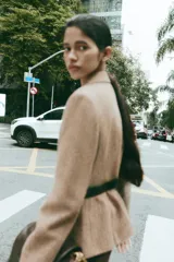 Blazer de corte clásico con cuello solapa y manga larga, confeccionado en tejido con patrón de espiga en tonos tierra y líneas verticales en color salmón. Cuenta con bolsillos delanteros y cierre frontal con botones ocultos.
