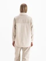 Camisa de manga larga color beige con diseño combinado, que incluye panel frontal de tejido texturizado, cuello clásico y cierre frontal de botones.