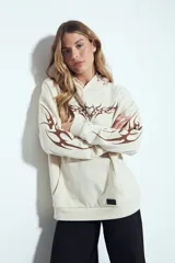 Canguro color beige de silueta relajada con capucha integrada, bolsillo canguro y terminaciones clásicas. Presenta una estampa frontal con un diseño tribal en color marrón y detalles gráficos a juego en las mangas.