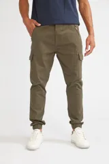 Pantalón cargo de corte slim, color verde oliva, con bolsillos laterales tipo cargo, cierre frontal con botón y puños elásticos en los tobillos.