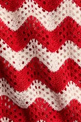 Top sin mangas de punto jacquard estilo crochet con patrón en zigzag de franjas rojas y blancas, cuello redondo y bajo levemente acampanado.