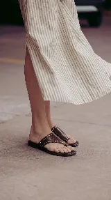 Sandalias chatas de cuero color bordó, con diseño de tira ancha que envuelve el empeine y sujeta el dedo gordo, decoradas con tachas metálicas doradas.