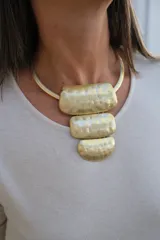 Collar rígido de metal dorado con diseño de gargantilla y tres dijes colgantes de formas rectangulares y semicirculares con acabado martillado.