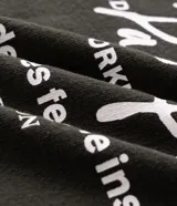 Remera de corte oversized color verde oscuro, con cuello redondo y mangas cortas. Presenta un diseño estampado en la espalda con tipografía en blanco y un pequeño logo gráfico en la parte inferior.