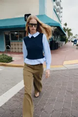 Camisa de popelín celeste con cuello solapa y manga larga, combinada con un chaleco de punto trenzado en color azul marino superpuesto. Presenta un diseño de capas con cierre en la espalda mediante botones ocultos.