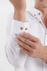Camisa de vestir blanca de manga larga, con cuello abotonado, bolsillo frontal y botones en tono madera.
