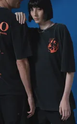 Remera de manga corta con cuello redondo y calce oversize, color negro con efecto nevado. Presenta una estampa frontal en color naranja con diseño gráfico de un rostro rodeado de llamas y texto tipográfico.