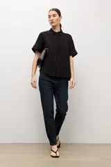 Camisa negra de manga corta, con cuello camisero clásico y cierre frontal de botones.