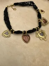 Gargantilla de encaje negro con cadena de ajuste dorada, decorada con múltiples dijes en forma de corazón con detalles metálicos dorados y centros en tonos rosados y grisáceos.