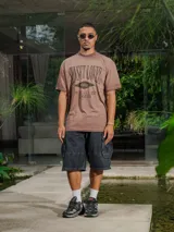 Remera de jersey con efecto teñido, color marrón, de corte holgado y cuello redondo. Presenta un estampado frontal con texto en tonos más oscuros.