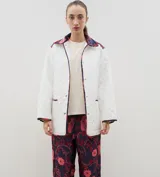 Campera acolchada de corte holgado, color blanco con diseño capitoneado en forma de rombos. Presenta cuello camisero y bordes internos con estampado floral en tonos azul y rojo, cierre frontal con botones a presión y bolsillos laterales.