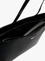 Bolso tipo tote de Tommy Jeans en color negro con acabado brillante. Presenta un diseño minimalista con doble asa superior y el logo distintivo de la marca aplicado en la parte frontal.