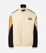 Campera de sarga de algodón marca Blue Steel, con diseño de bloques de color en tonos beige, negro y mostaza. Presenta cuello alto, cierre frontal con botones a presión y solapa, bolsillos laterales y detalles de parches bordados con temática outdoor en el pecho y la manga.