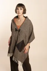 Chal de lana fina sin teñir con diseño de cuadros sutiles, cierre frontal con alamar y bolsillos de cuero metalizado. Presenta terminaciones con flecos en el ruedo y un calce estructurado en los hombros.