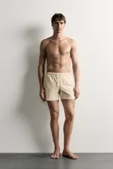 Short de baño de tejido técnico en color beige con estampado paisley en tonos claros y naranjas. Cuenta con cintura elástica con cordón ajustable, bolsillos laterales y forro interior.