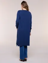 Cardigan largo de punto liviano y suave, de color blanco, con diseño abierto al frente, mangas largas con puños acanalados y bolsillos frontales aplicados.