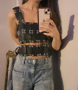 Top tipo armadura o corsé, confeccionado con tiras superpuestas de material blanco perforado (tipo puntillado) unidas entre sí mediante argollas metálicas. Presenta un diseño personalizable en color, textura y forma (Halter, Cuello cuadrado o Cuello en V).