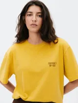 Camiseta de corte oversized color amarillo, con cuello redondo, mangas cortas y estampa pequeña en el pecho con el texto (DESDE) 18-80.