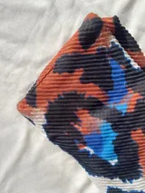 Pañuelo rectangular de textura plisada con estampado abstracto en tonos tierra, negro y azul.