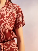 Mono corto negro con estampado floral en tonos beige y amarillo. Presenta cuello camisero, manga corta y un lazo ajustable en la cintura.