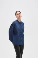 Camisa de jean azul con cuello mao, cierre frontal con botones y mangas largas con puños elásticos fruncidos.